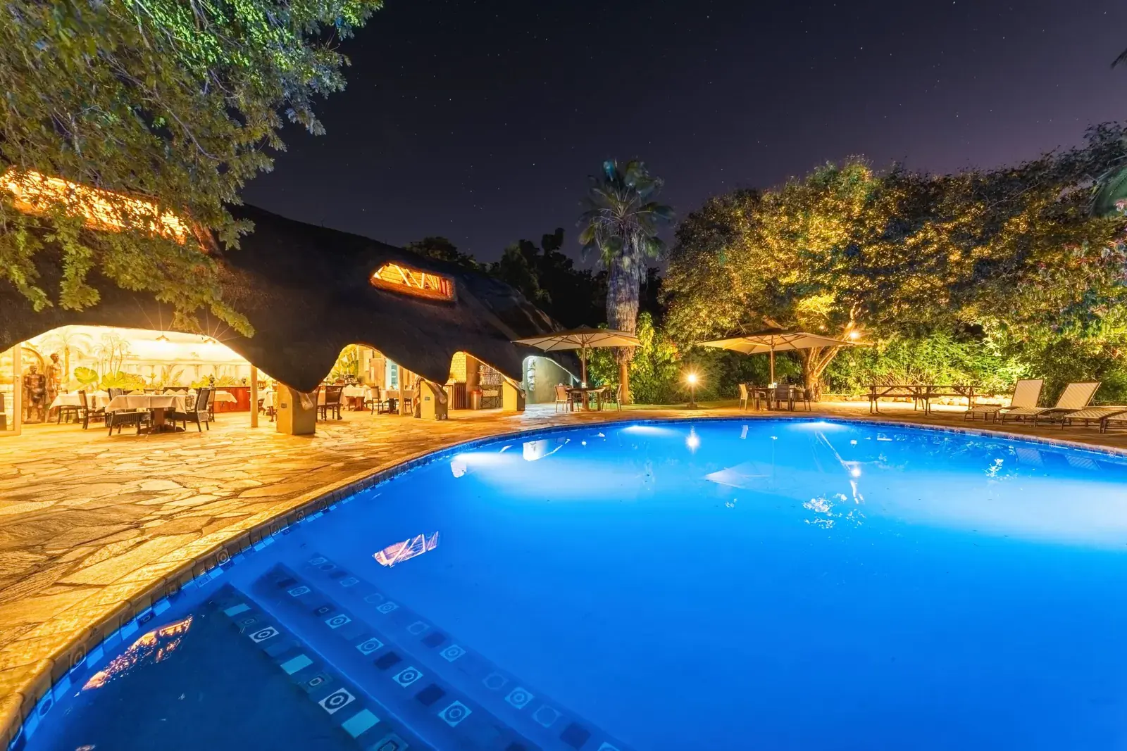 Bayete Guest Lodge pool lit up at night, with thatched buildings behind