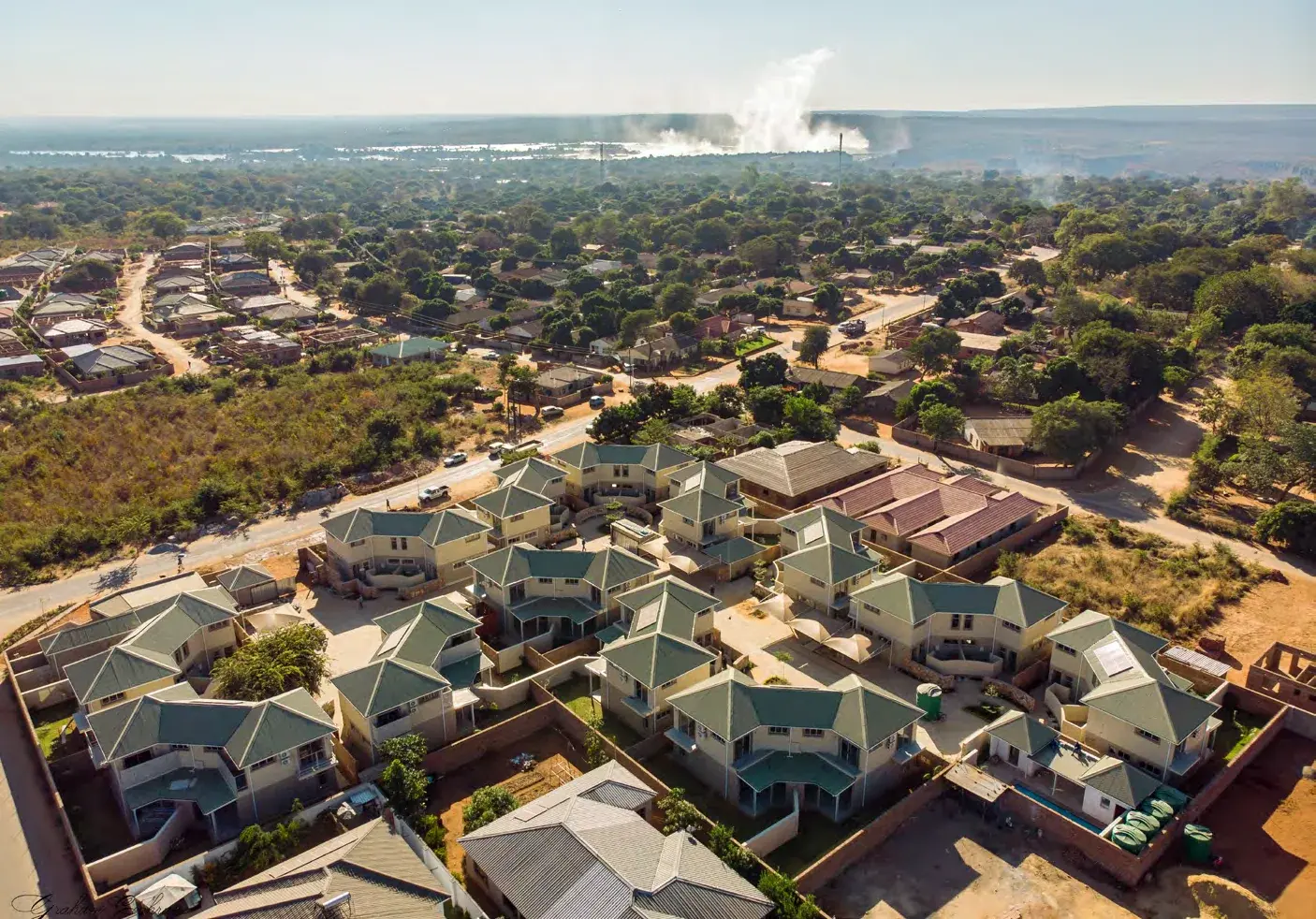 Aerial view of the Miombo Mews villas in Victoria Falls, with spray from the Falls on the horizon