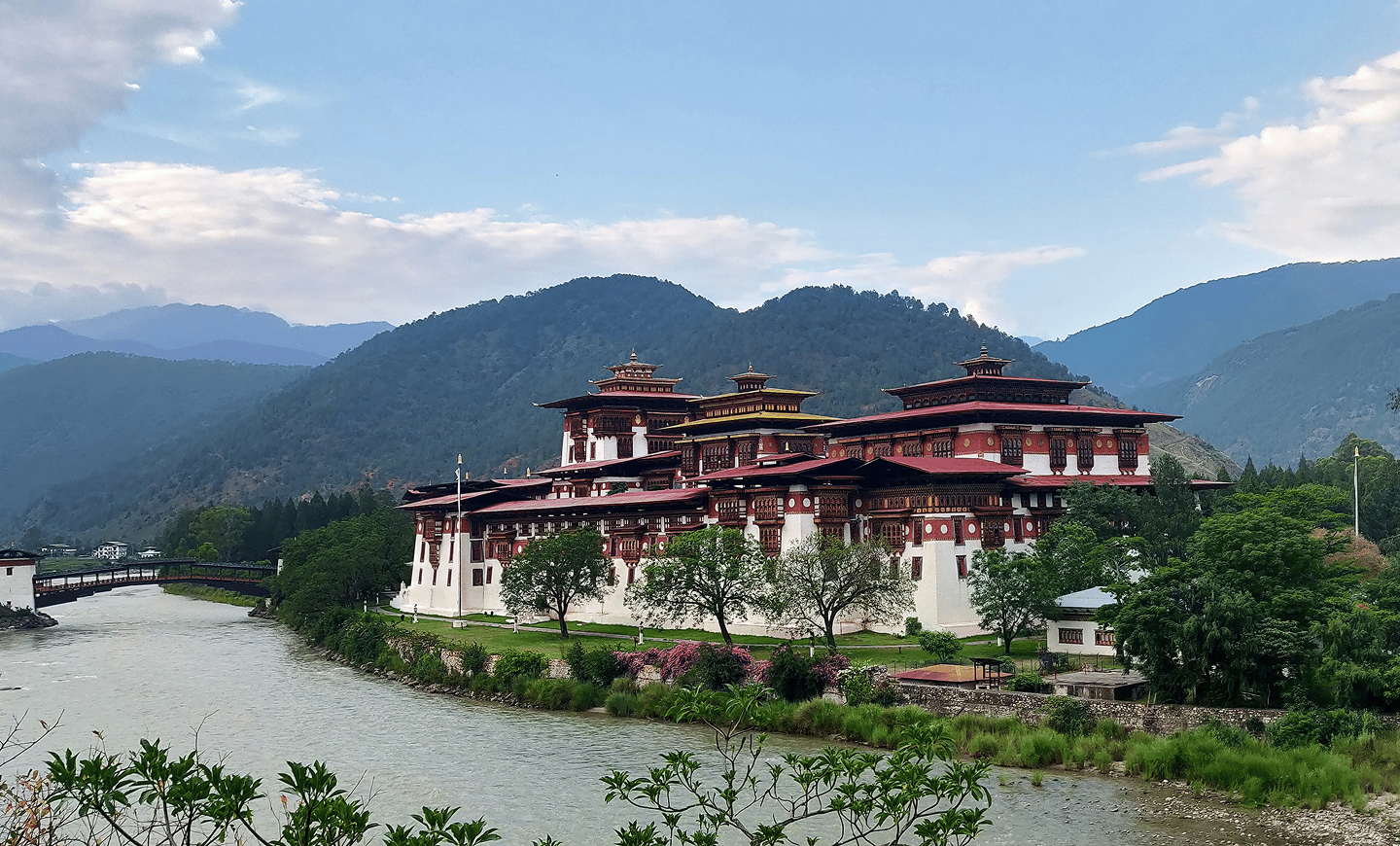 Large whitewashed fortress beside a river, with forested hills behind