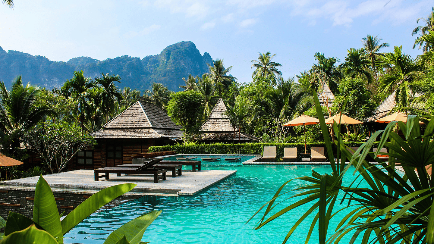 Resort pool surrounded by thatched buildings and palms